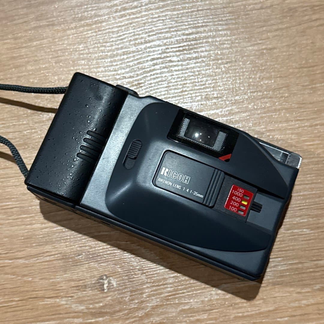 A vintage Ricoh point-and-shoot 35mm film camera.