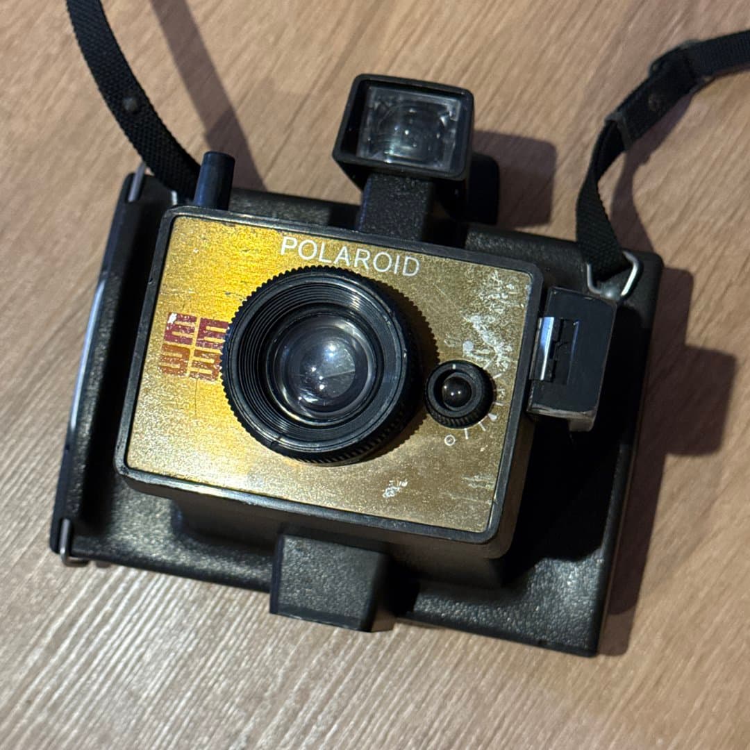 Vintage Polaroid EE33 instant camera with a gold faceplate and black strap, showing signs of age.