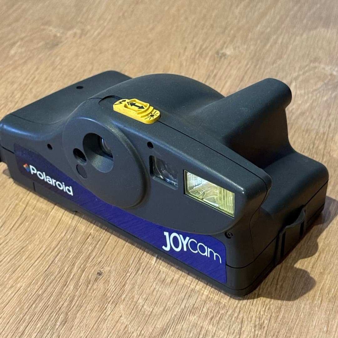 Dark grey Polaroid JOYcam instant camera with flash on a wooden surface.