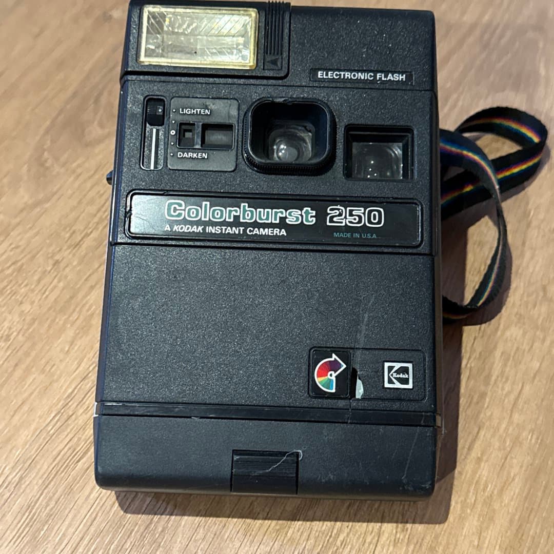 A vintage Kodak Colorburst 250 instant camera, featuring an electronic flash and a rainbow strap.