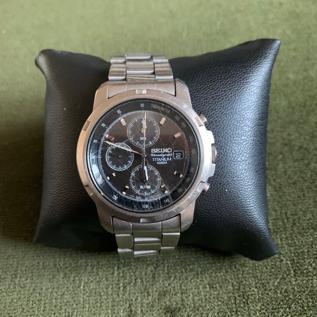 Seiko Chronograph Titanium 100M watch with black dial, metal bracelet, and tachymeter.