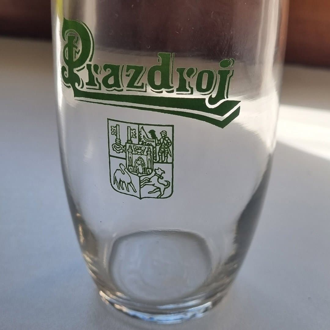 Prazdroj branded clear beer glass with green logo and coat of arms.