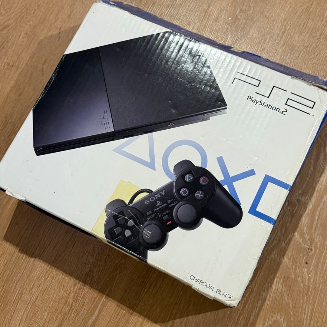 A classic Sony PlayStation 2 console in Charcoal Black, displayed on its original box.