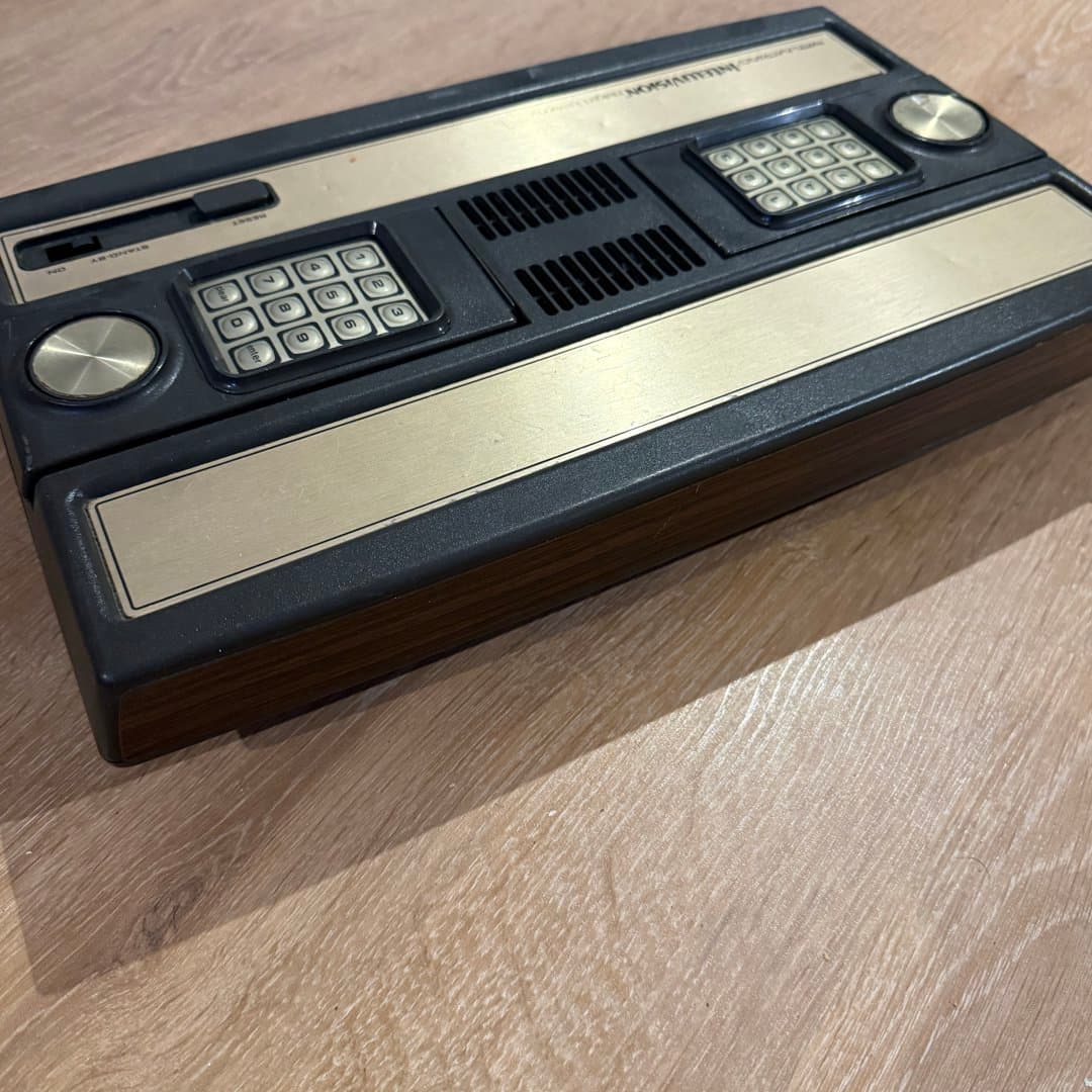 A vintage Intellivision video game console with a classic wood-grain and gold design.