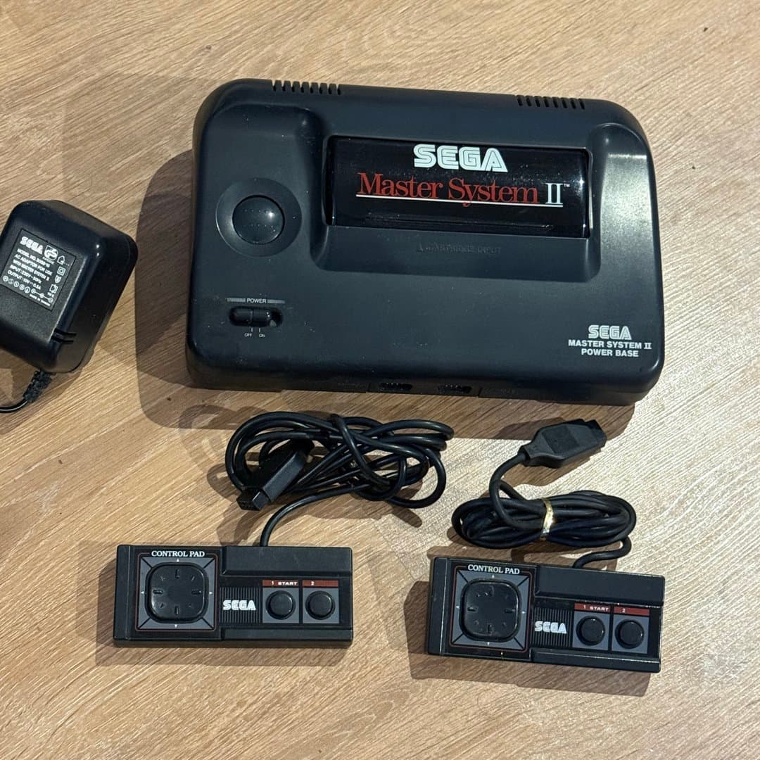 A vintage Sega Master System II console with two controllers and power adapter.
