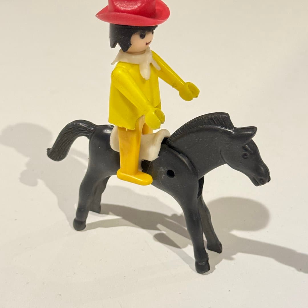 Pilsan cowboy figure with red hat riding a black toy horse.