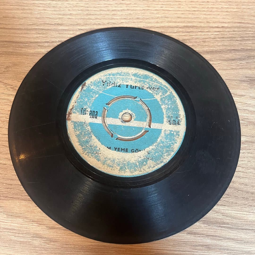 A vintage 45 RPM vinyl record with a worn blue and white label, featuring Turkish text.