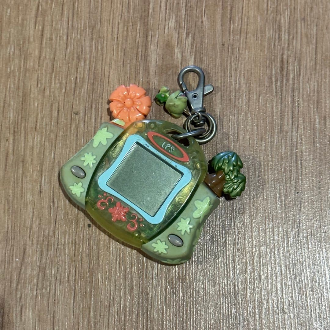 A vintage-style virtual pet keychain with a small screen and nature-themed decorations.