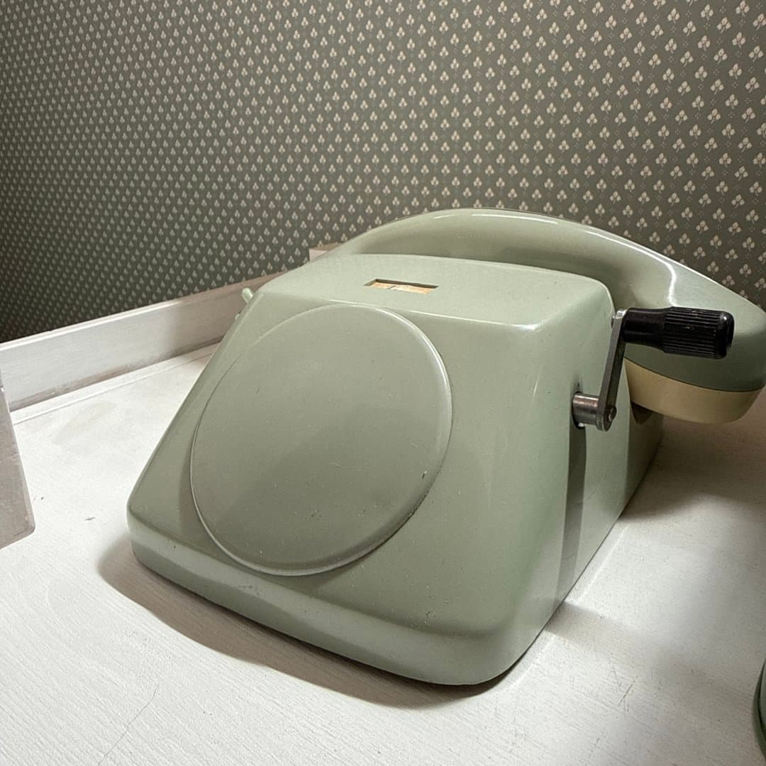 Vintage light green rotary telephone with a side crank handle.