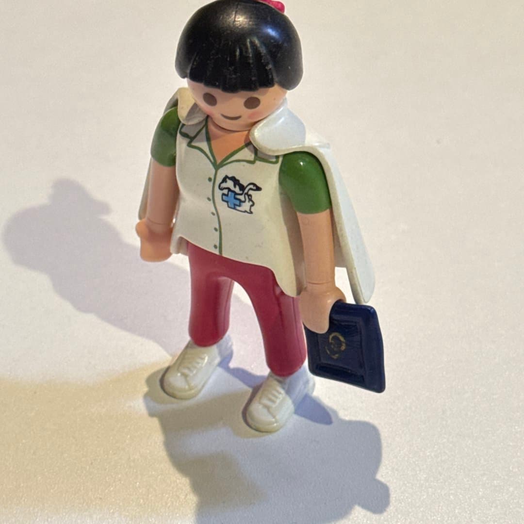 Playmobil Geobra 1992 female veterinarian figure with animal logo uniform and a blue book.